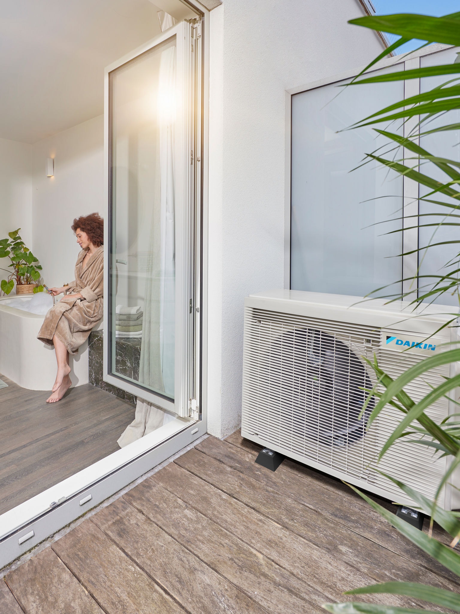 Air source heat pump installed beside terrace with open doors into a modern bathroom