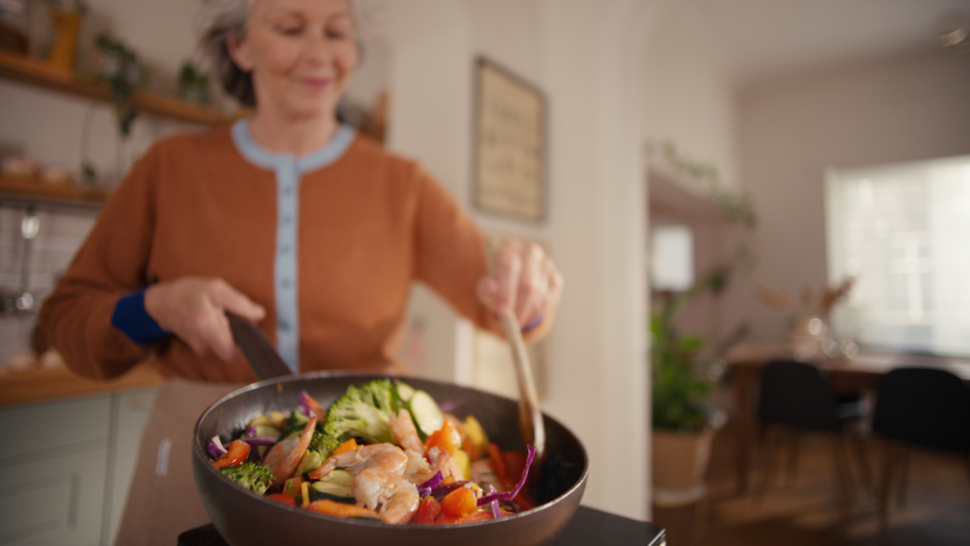 A smiling woman tossing a prawn stir fry in a frying pan and making kitchen odours