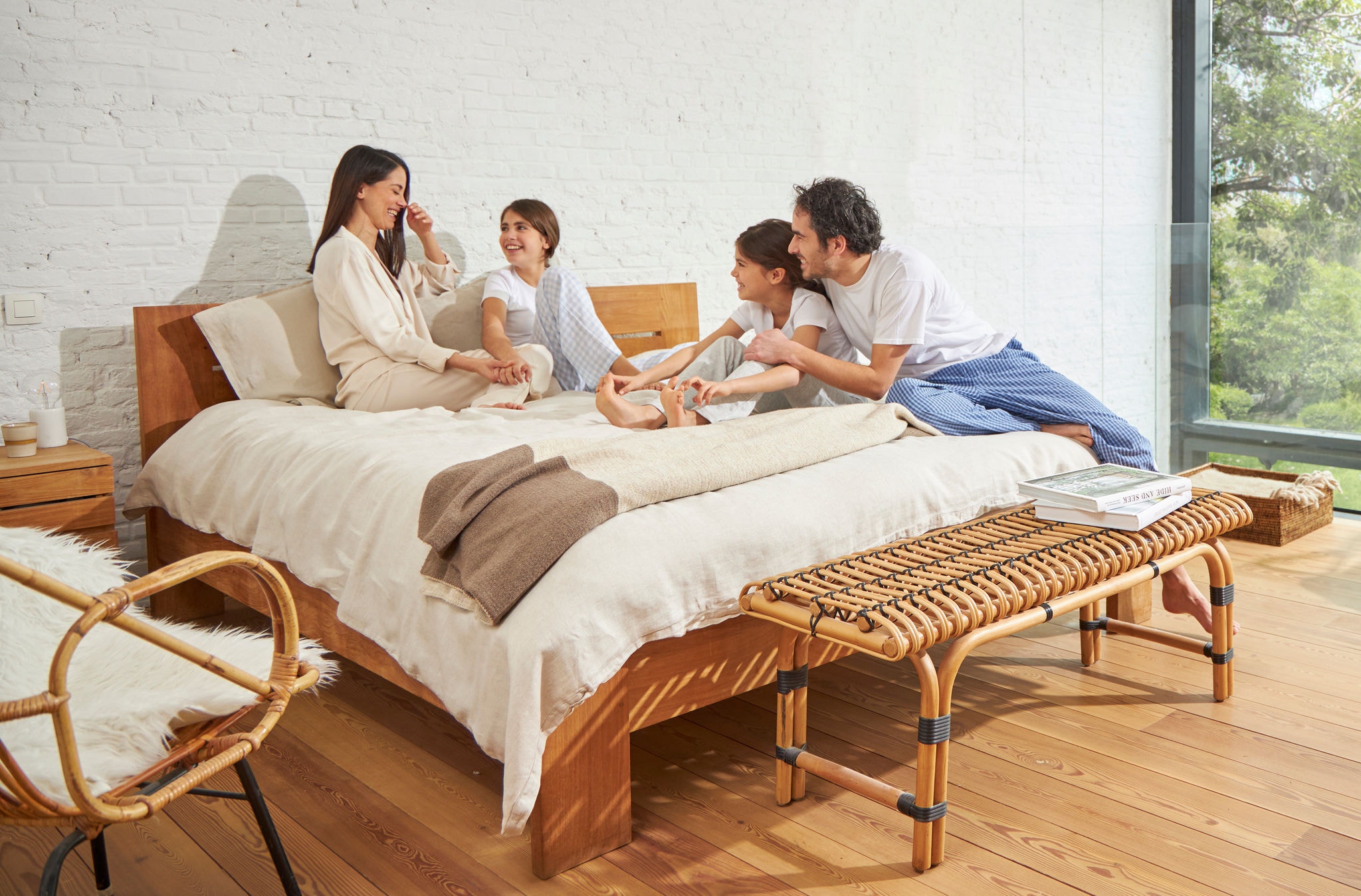 A woman and a man sitting on a bed with two young girls, relaxed, laughing and enjoying healthy air.