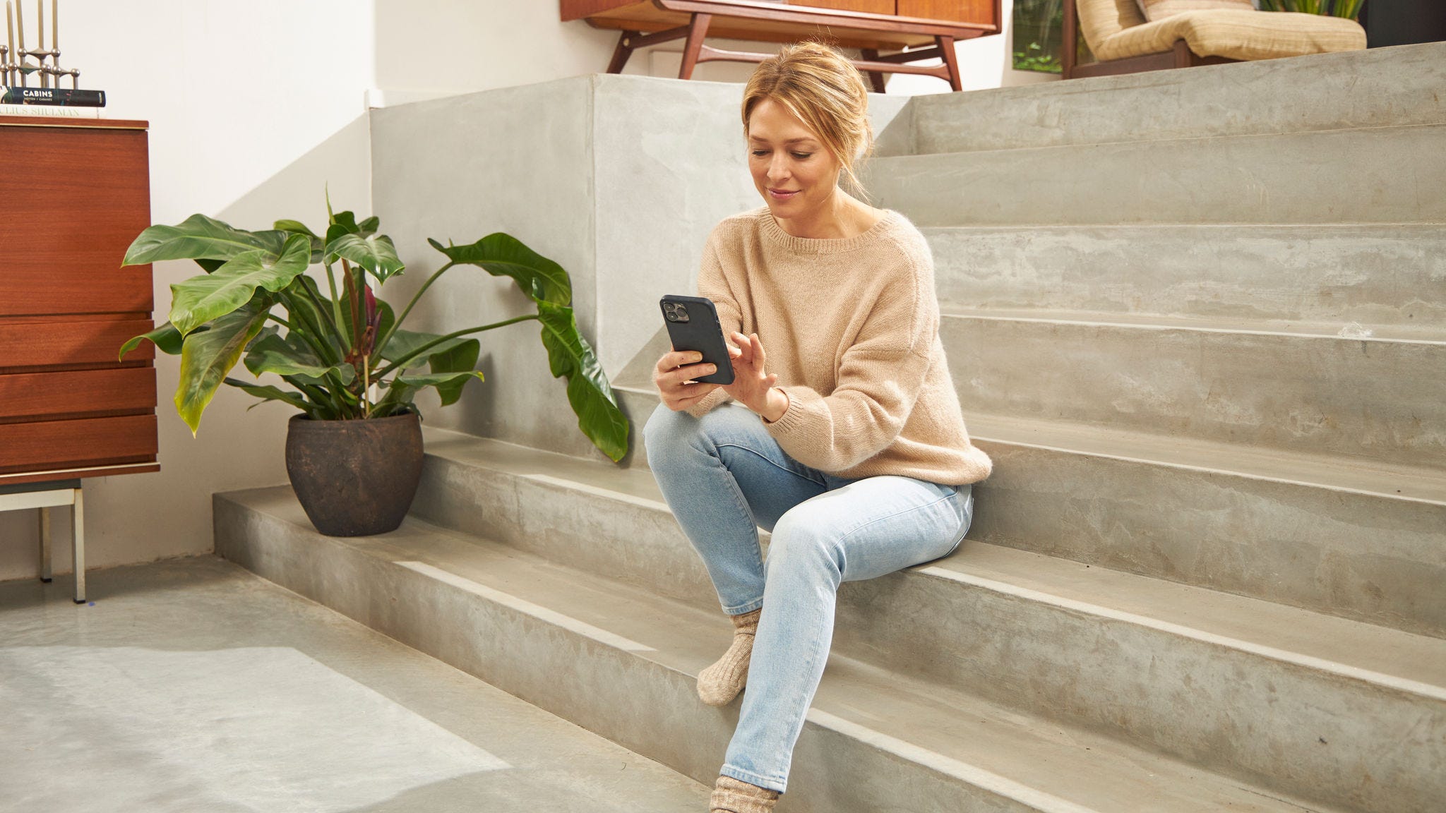 Woman sitting on steps in her home using the Onect app on her mobile phone