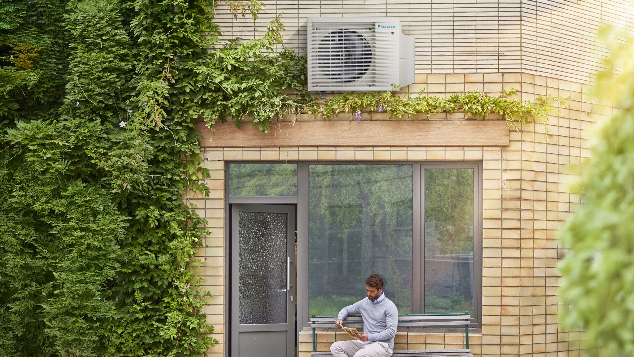 Man reading on a bench outside his house beneath a Daikin air source heat pump.