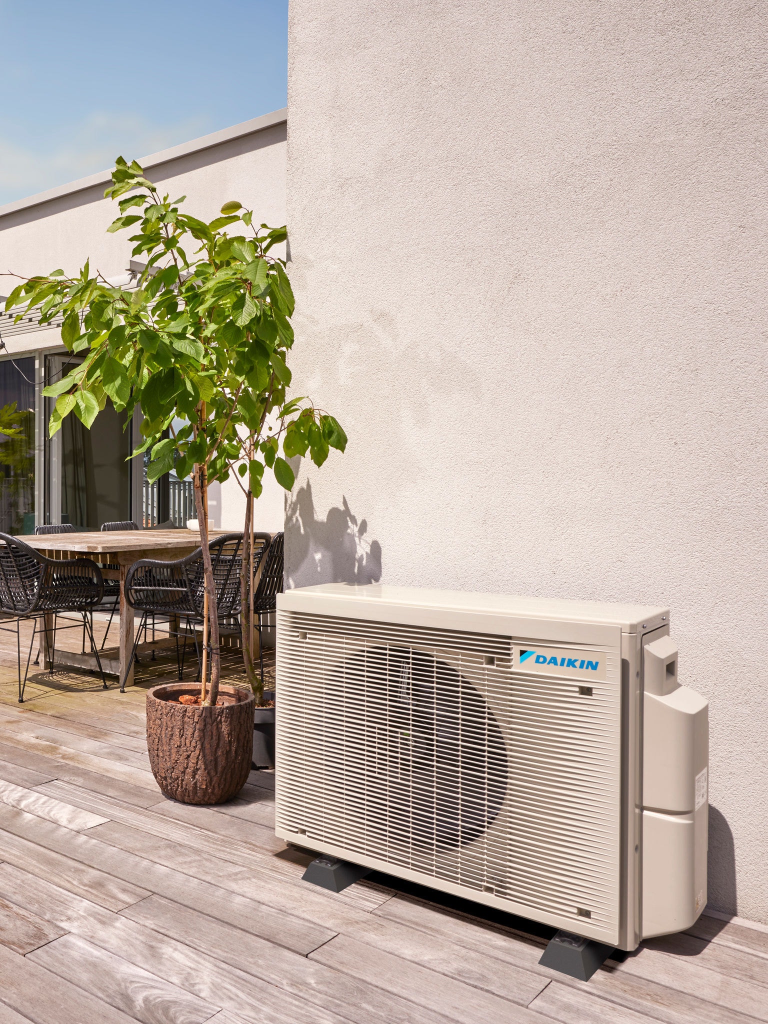 Outdoor heat pump positioned discreetly against a wall, shaded by trees