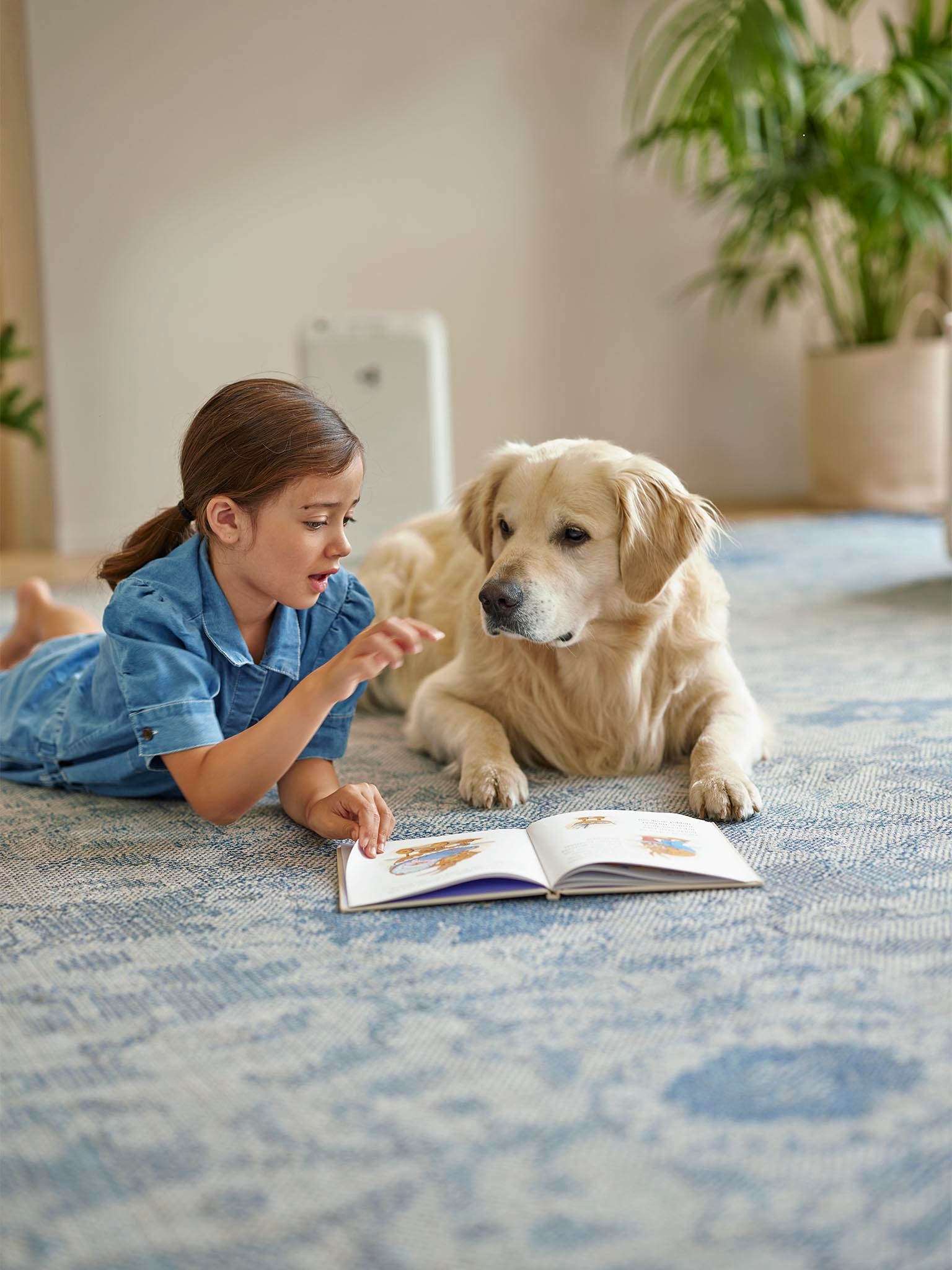 Girl lying next to dog on the floor while the air purifier is cleaning the air