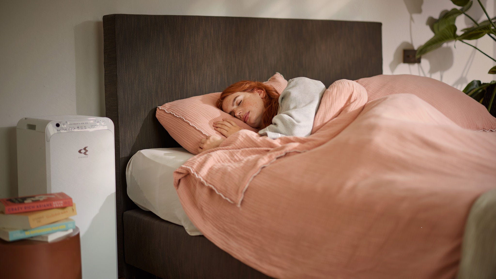 Woman peacefully sleeping in a cozy bed, while an air purifier operates nearby, ensuring clean air quality in a bedroom during winter