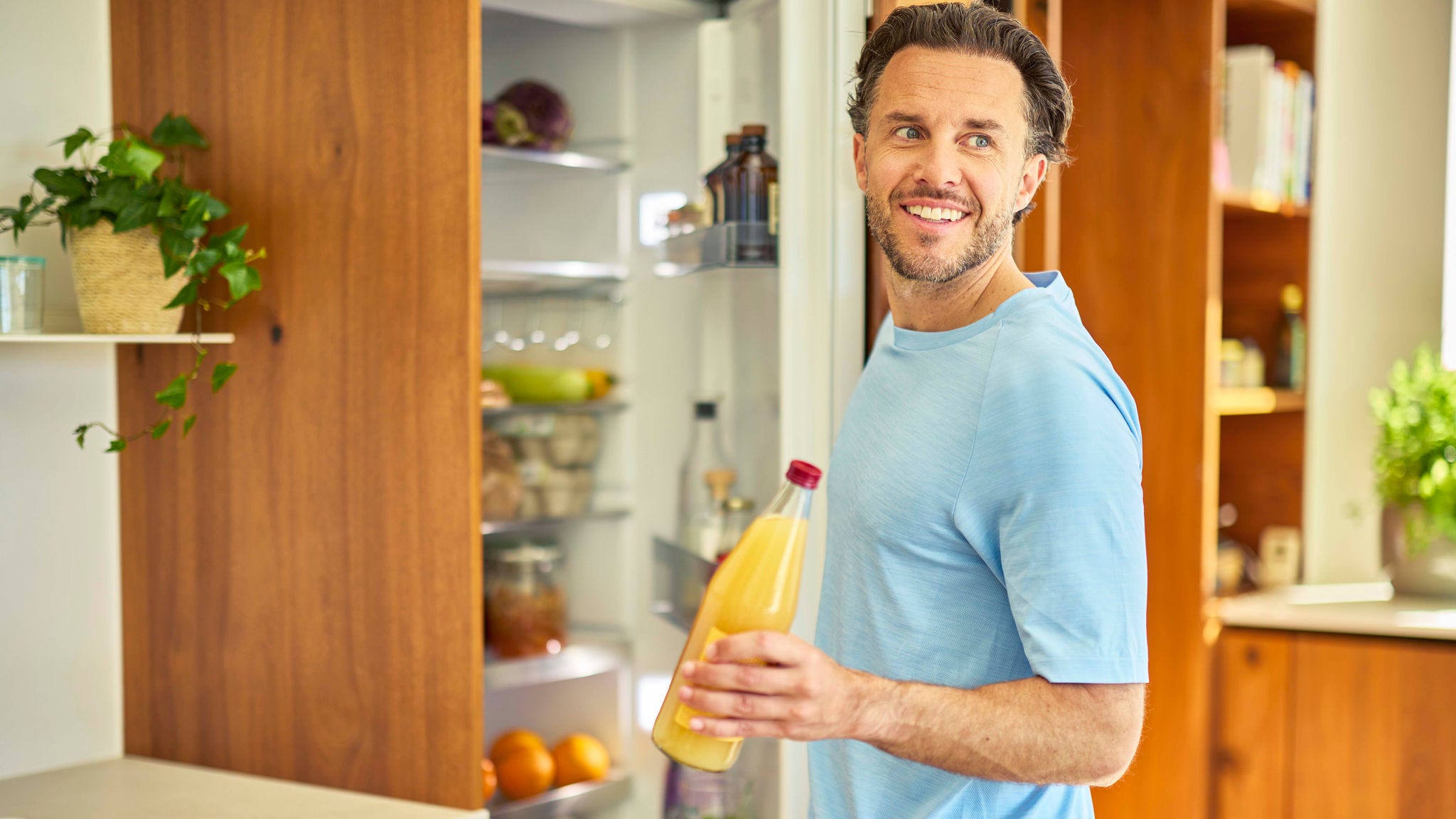 Man taking a bottle of orange juice from a refrigerator in a modern kitchen
