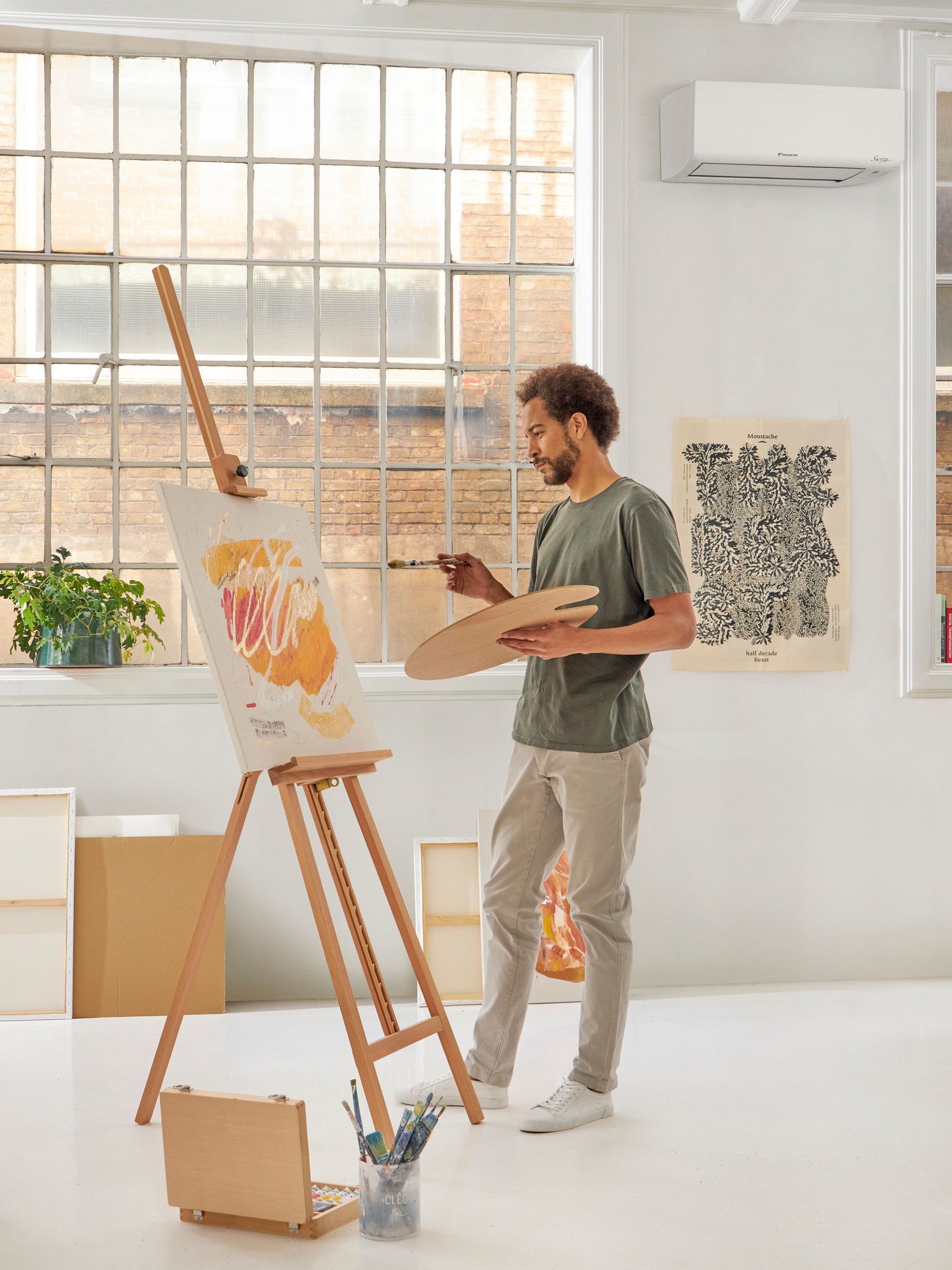 Man standing painting at an easel in a white room with a discreet white wall-mounted heat pump providing the perfect temperature
