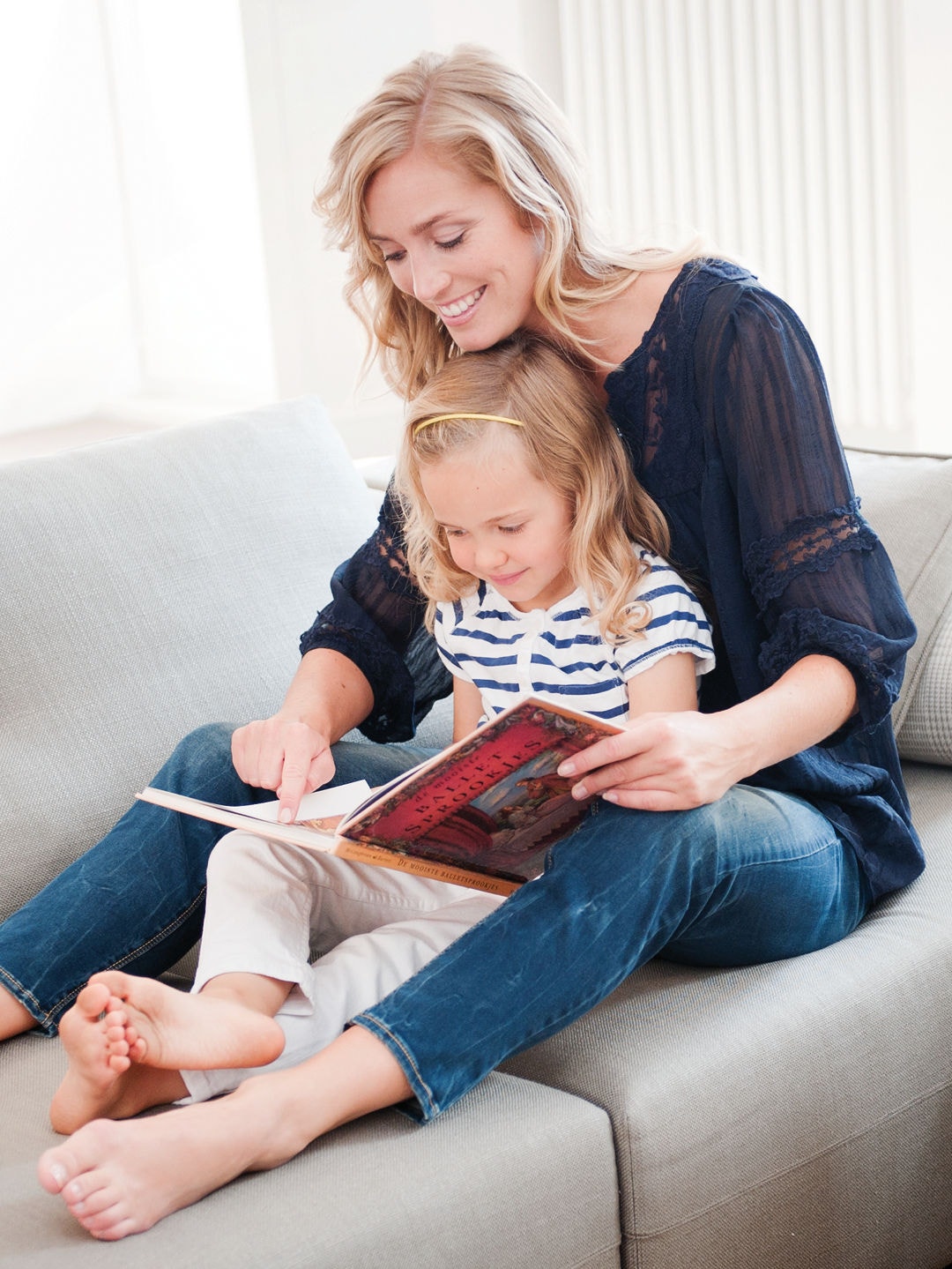 Little girl sitting in her mom's lap on the couch reading a book together in perfect temperature