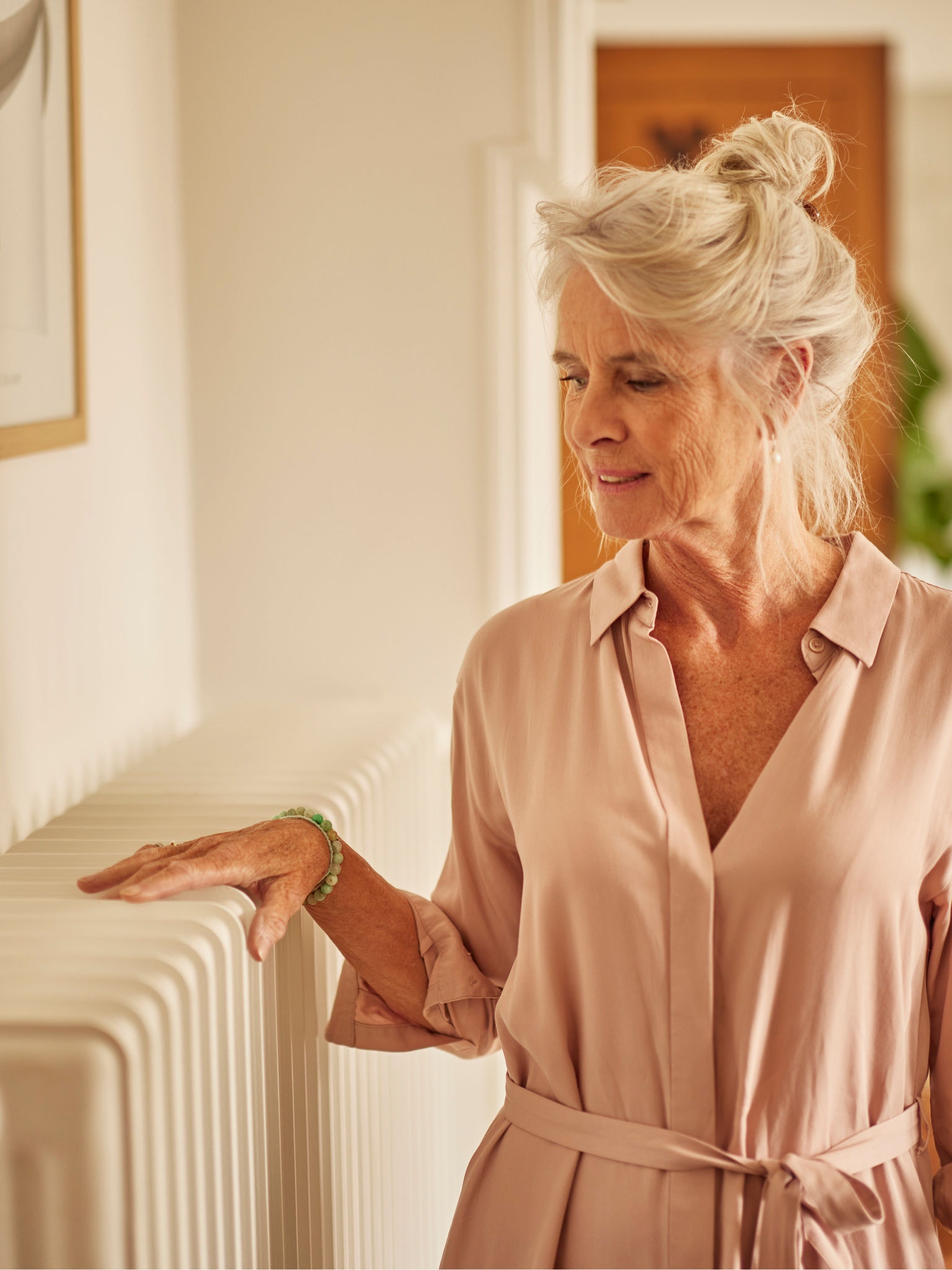 Woman warming hands on radiator paired with air source heat pump in bedroom