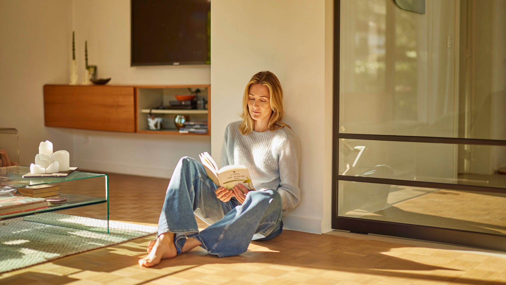 A women sitting, reading, on a wooden floor with underfloor heating, enjoying the perfectly heated room