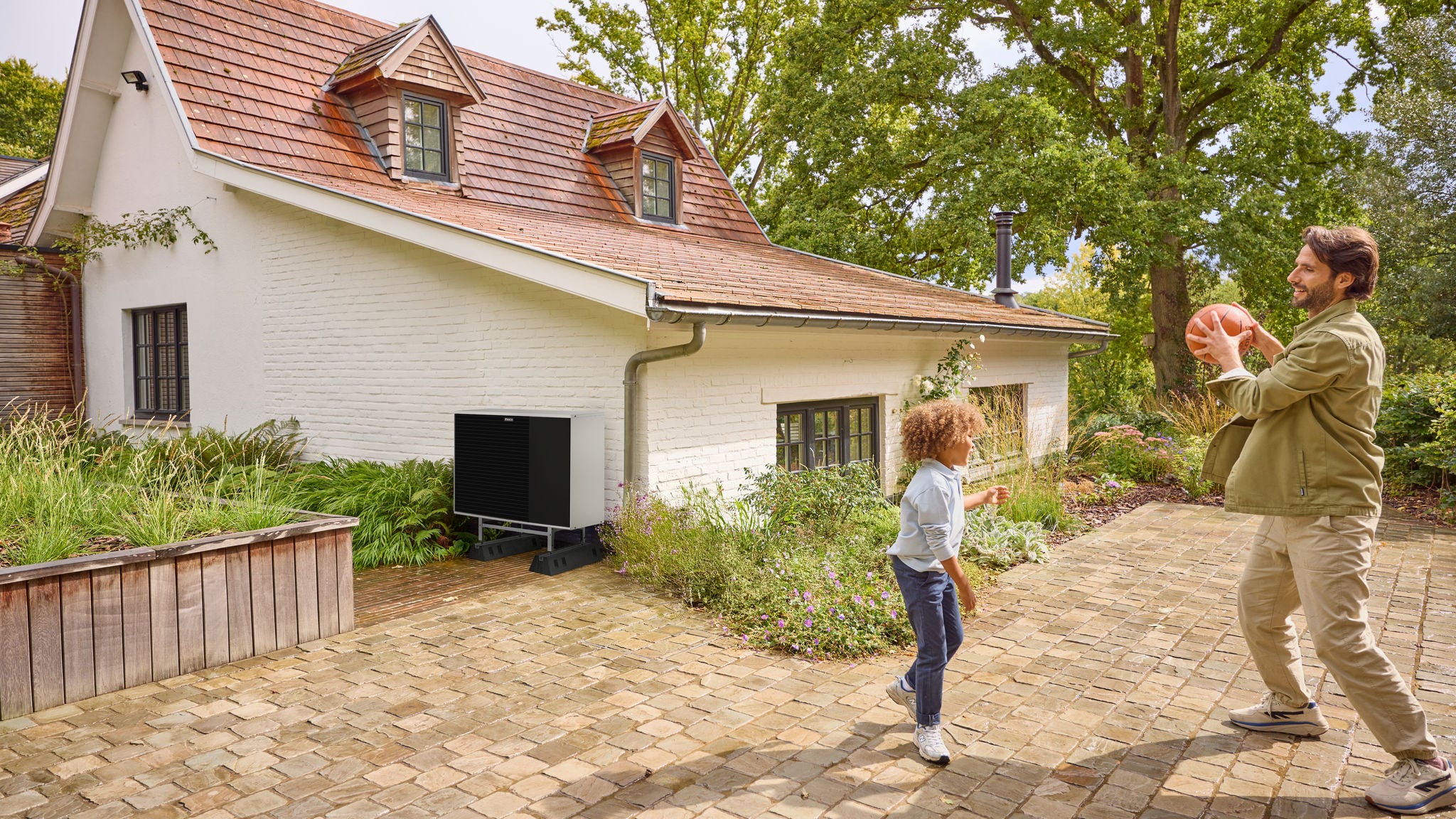 Father and son playing basketball near air source heat pump outdoor unit