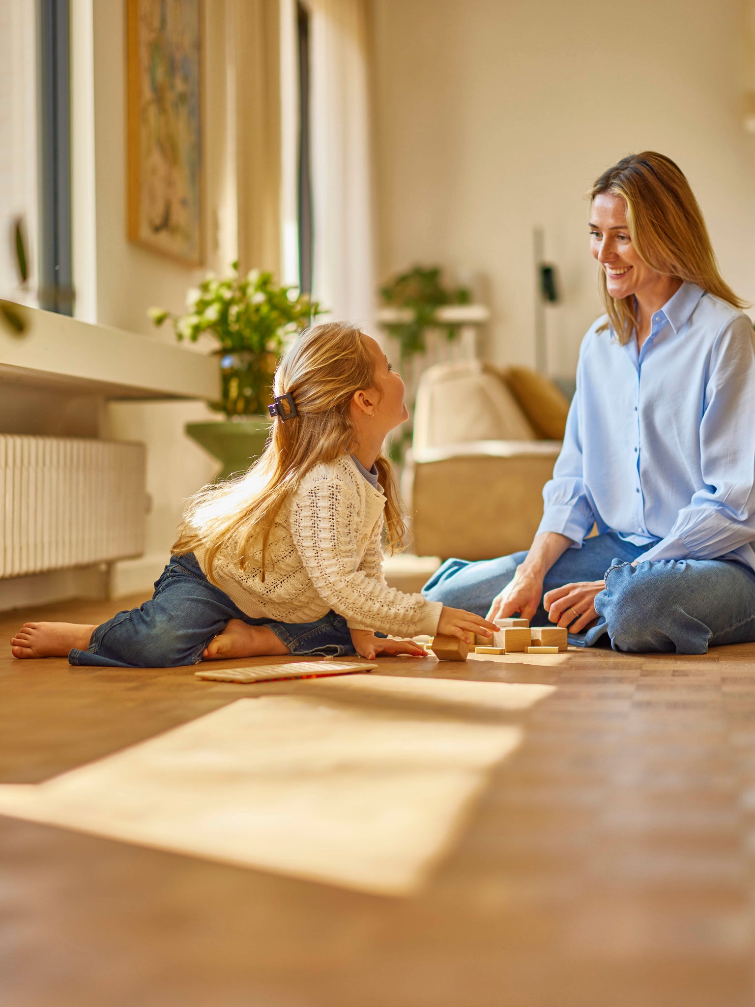 Mother playing with daughter in comfortably heated room with wall radiator