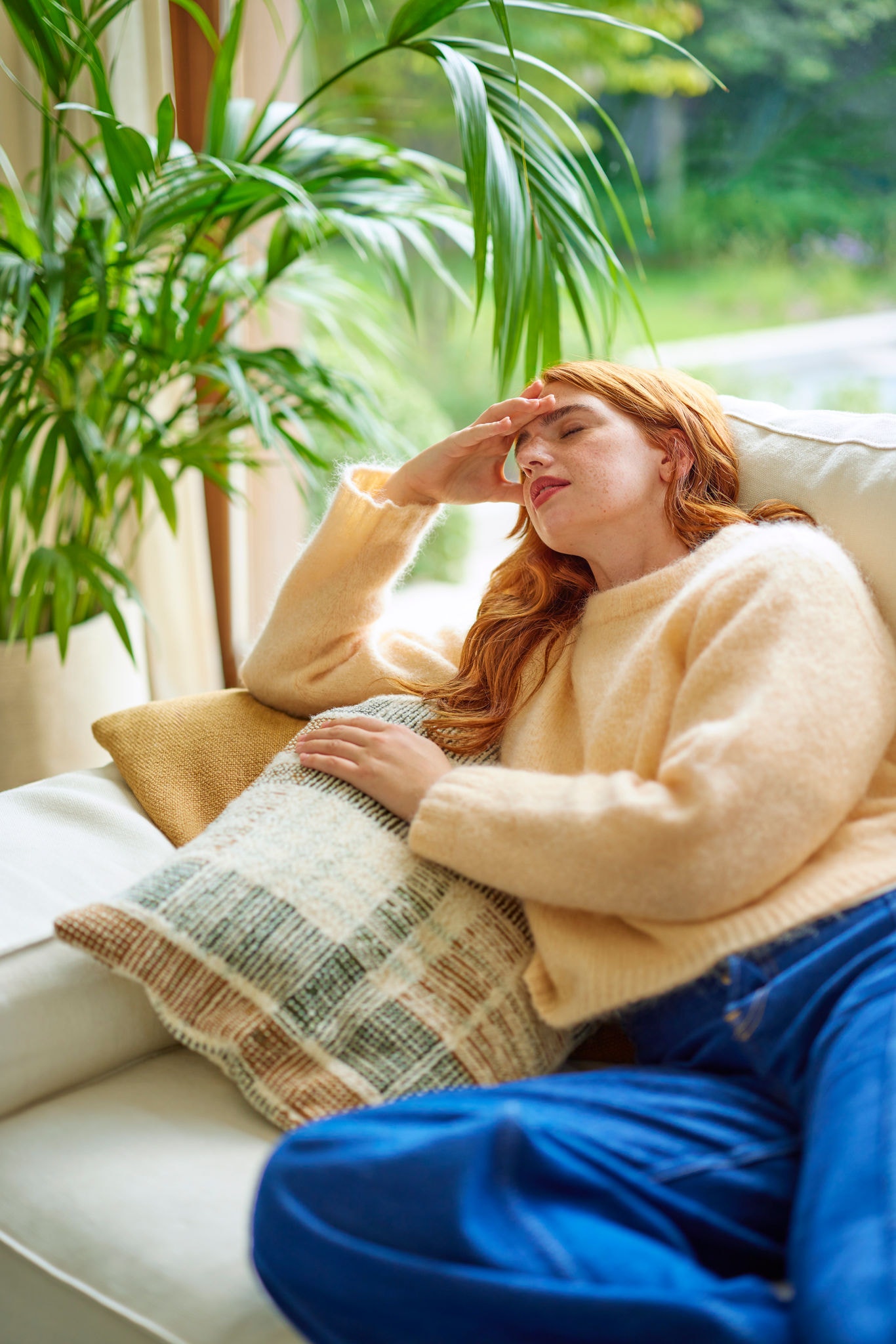 Girl feeling sick on sofa with headache, showing impact of poor air quality and need for proper ventilation
