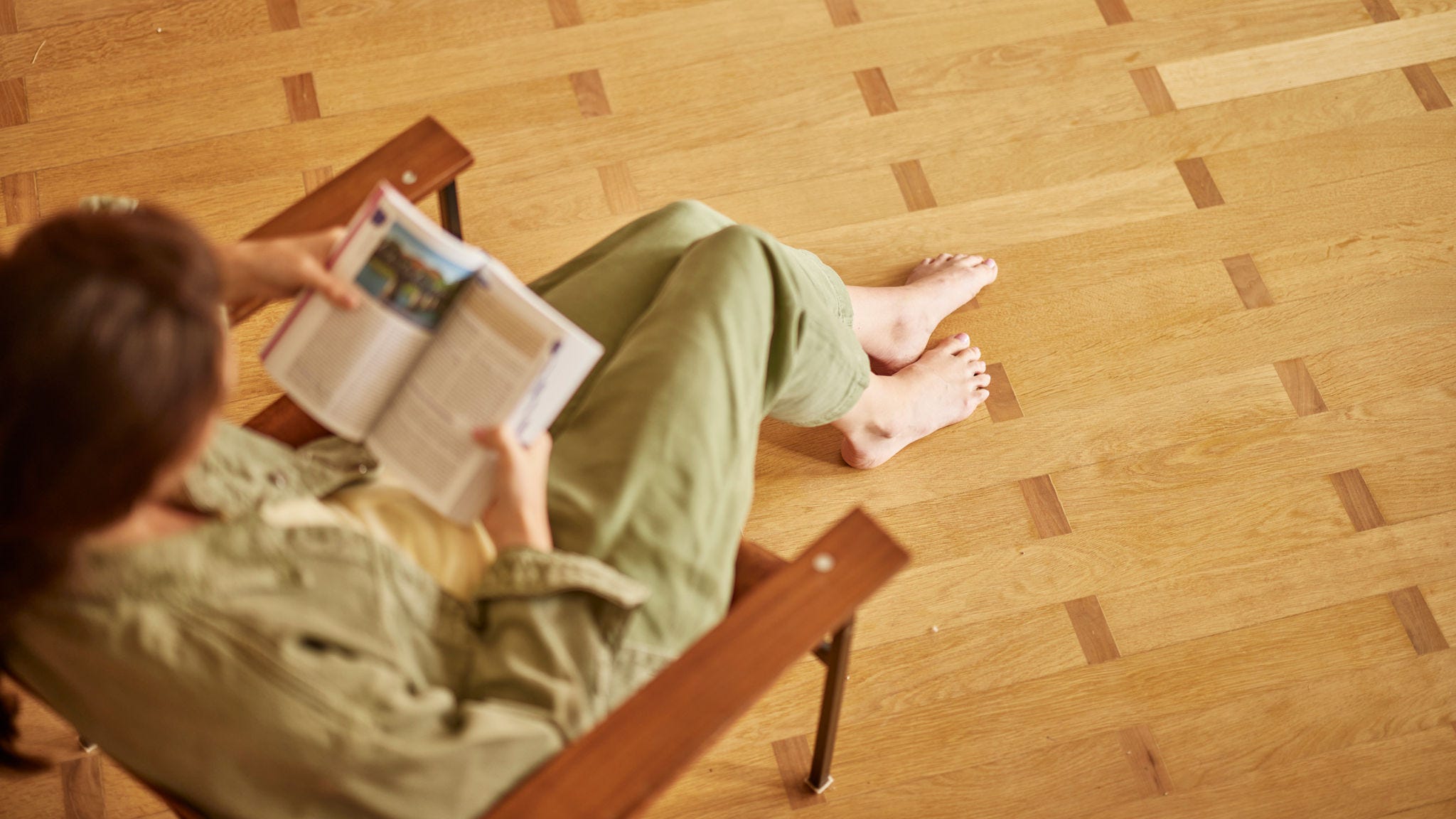 Woman sitting barefoot on a wooden floor enjoying the comfort of underfloor heating while reading a book