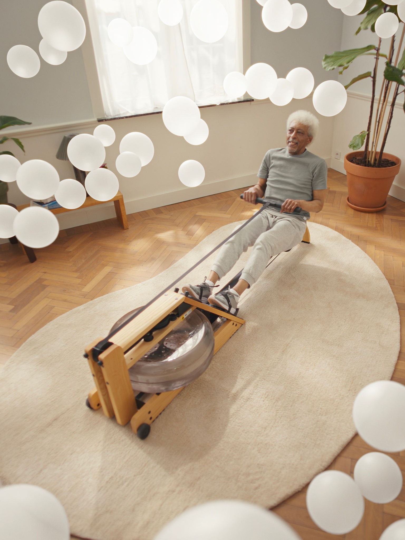 Older man exercising on a rowing machine in a clean-air environment, supported by an air purifier