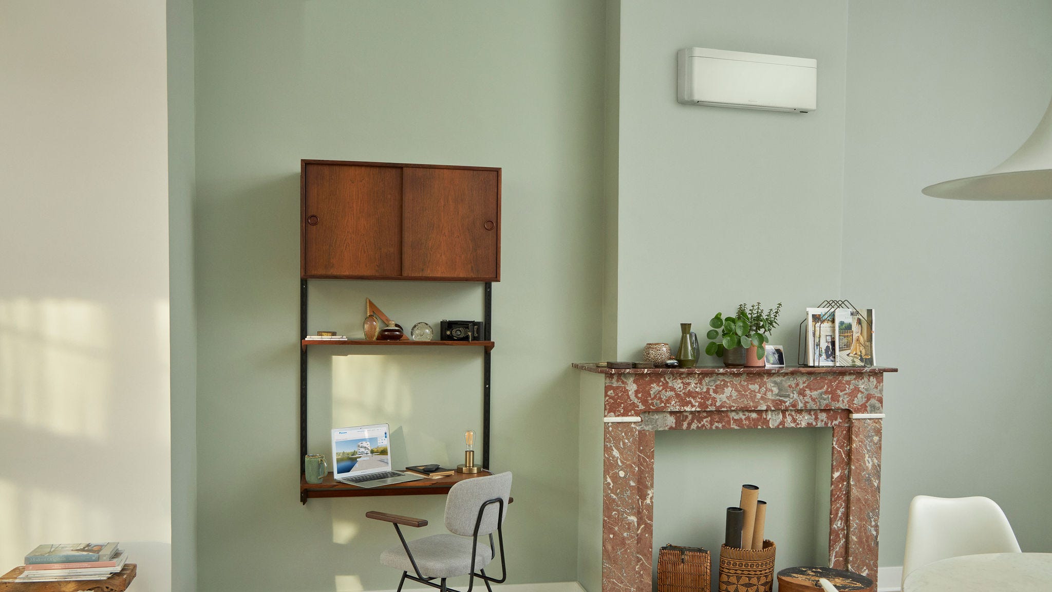 Discreet wall-mounted heat pump in a room with sage green walls above a decorative shelf