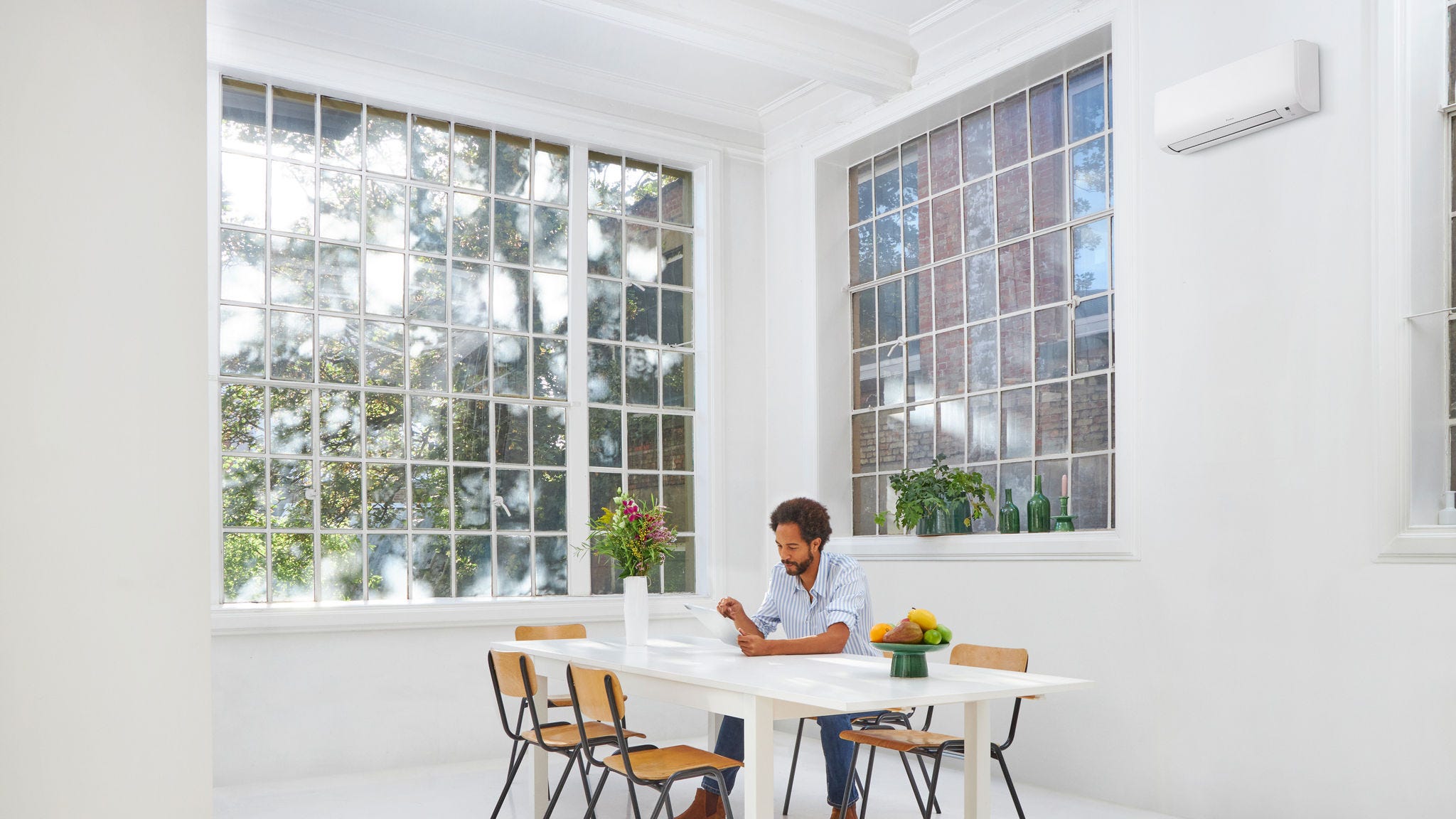 Man sitting in a bright, air-conditioned living space with large windows and natural light