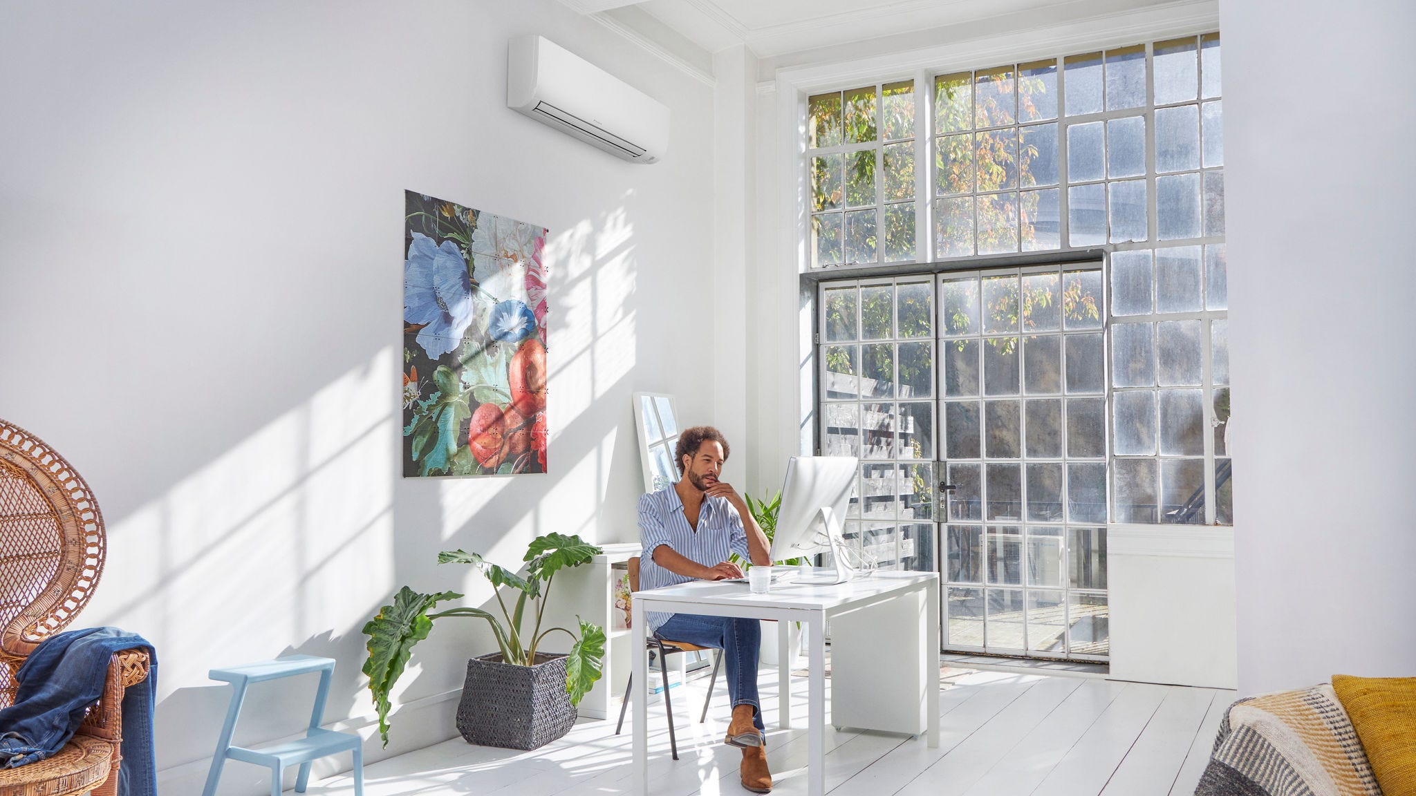 Man sitting inside a white room with a discreet wall-mounted heat pump blending in
