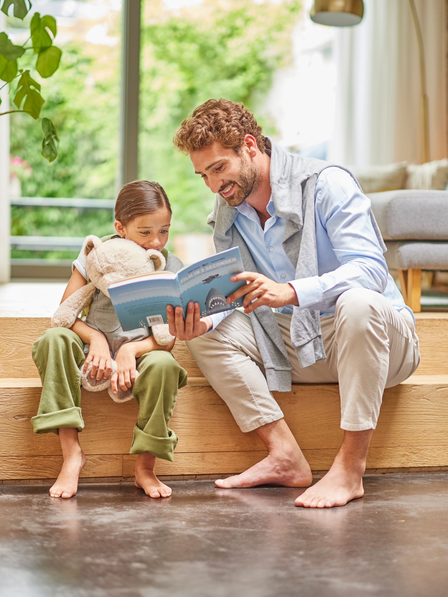 Father reading a book to his child, both sitting barefoot on the floor