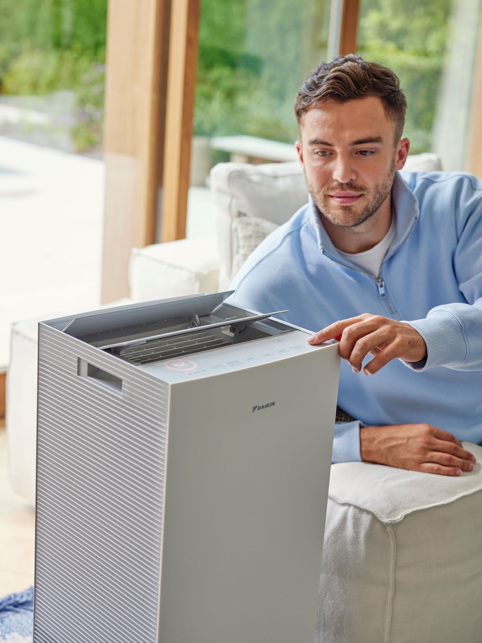 Man sitting on sofa in living room adjusting the controls of Daikin air purifier