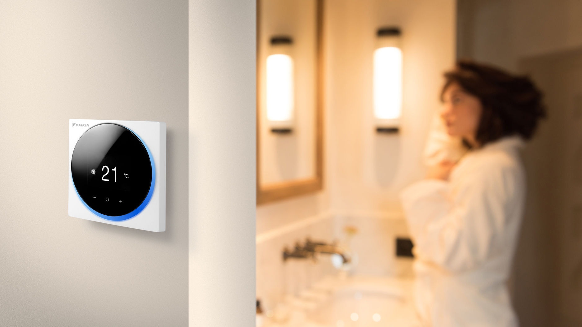 Woman standing in a bathroom next to a room with a wall-mounted compact wired room thermostat